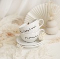 Zestaw 2 Białych Filiżanek Porcelanowych ze Spodkami 250 ml - Napis I Ślubuję Ci Uśmiech Przy Porannej Kawie dla Pary na Ślub Zbliżenie na złote zdobienie na białym filiżance porcelanowej 2 Białych Filiżanek Porcelanowych ze Spodkami 250 ml -